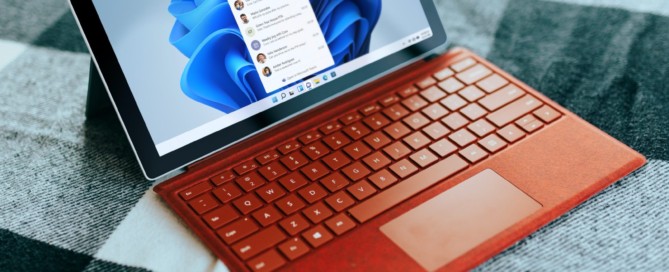 Red Surface laptop on a checkered bed by a window